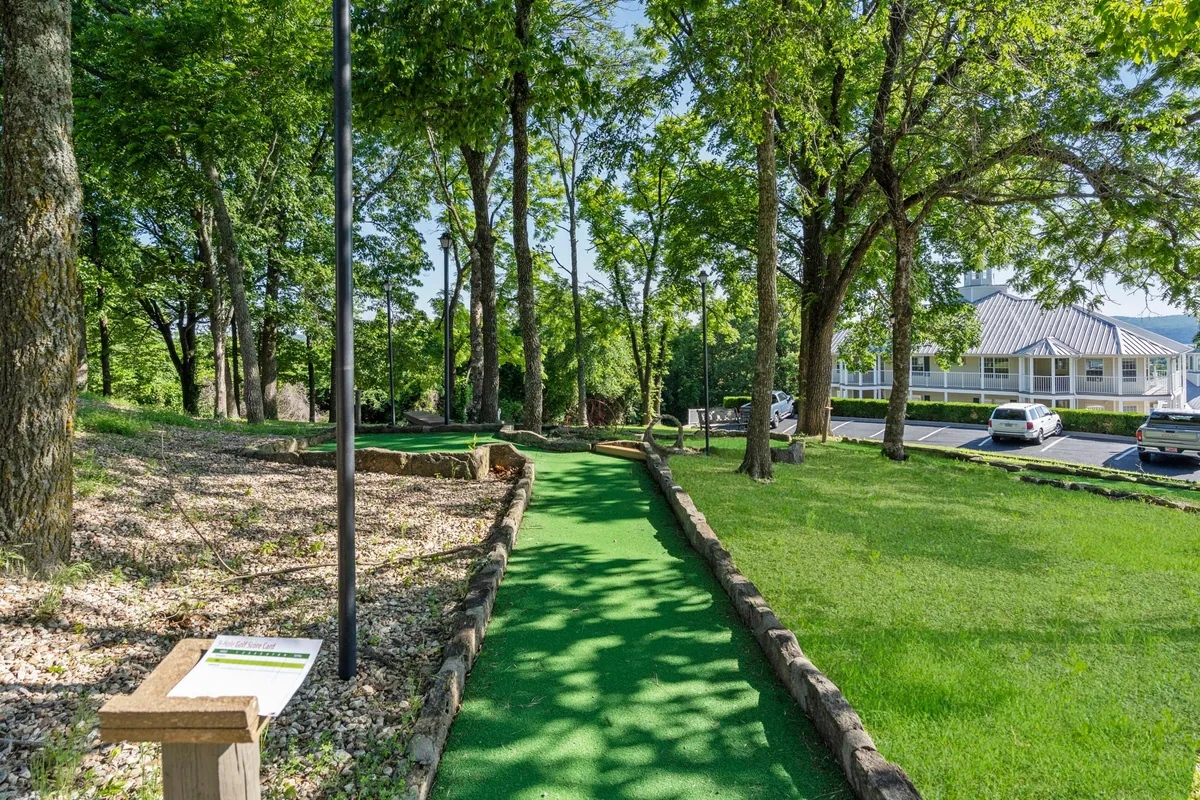 A playful mini-golf course surrounded by lush greenery, with clear signage and a nearby parking lot. The site offers a cheerful atmosphere perfect for family competition and outdoor enjoyment.