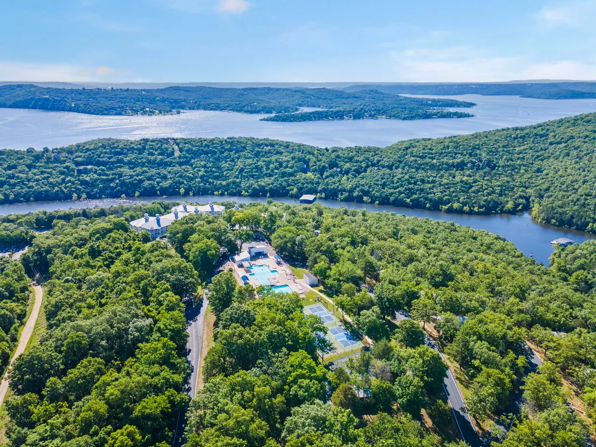 A panoramic view showcases the resort’s lush greenery, pool, tennis courts, sparkling lake, and winding road, capturing both amenities and the scenic Ozark setting in one expansive shot.