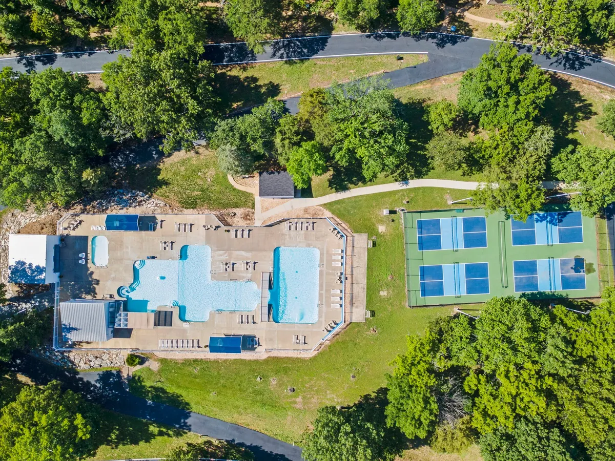 A spacious swimming pool sits at the center of a well-landscaped resort area, bordered by greenery and tennis courts. The setting is leisurely, with both sunbathing and active options available, reflecting the range of experiences possible at the resort.