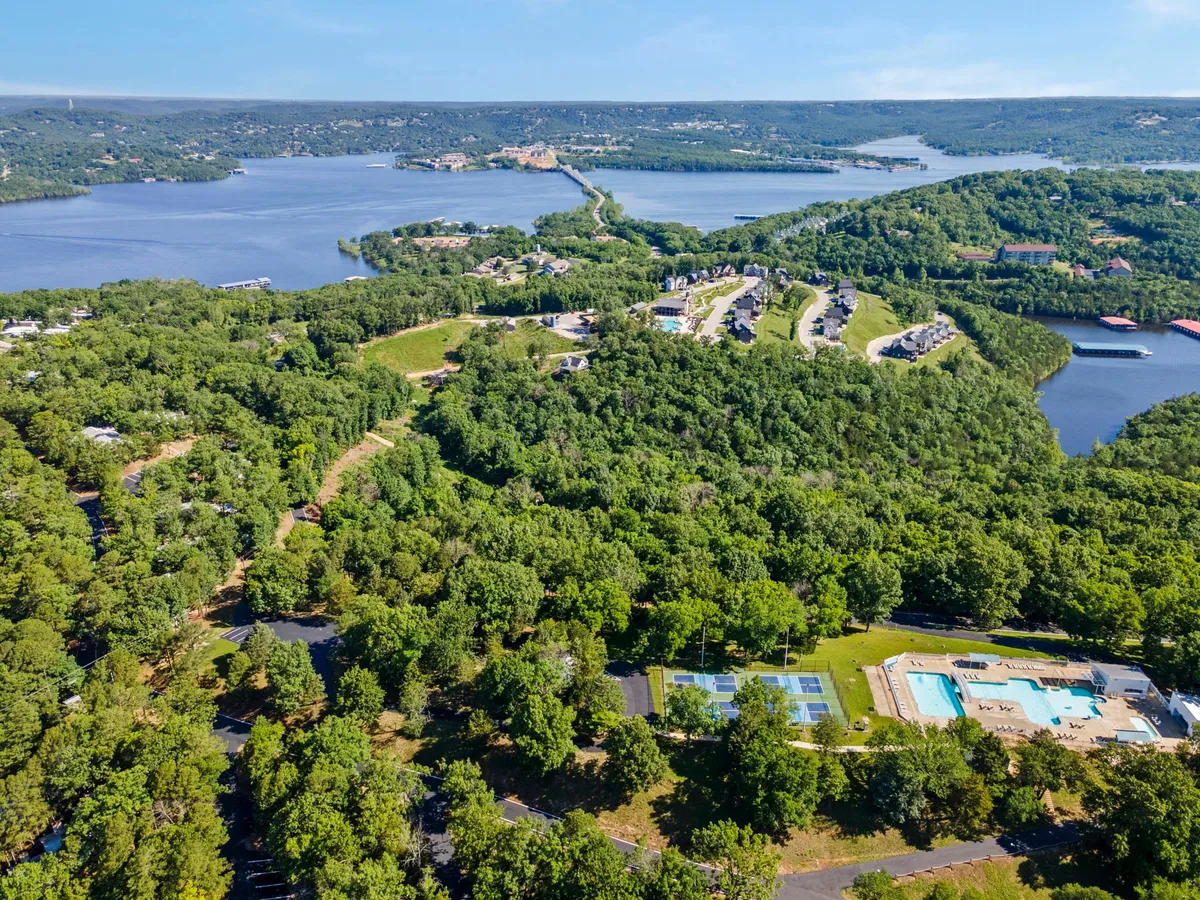 A sweeping view over lush greenery, a sparkling lake, a swimming pool, tennis courts, and winding roads. The landscape radiates serenity and outdoor activity opportunities, all in a pet-friendly setting.
