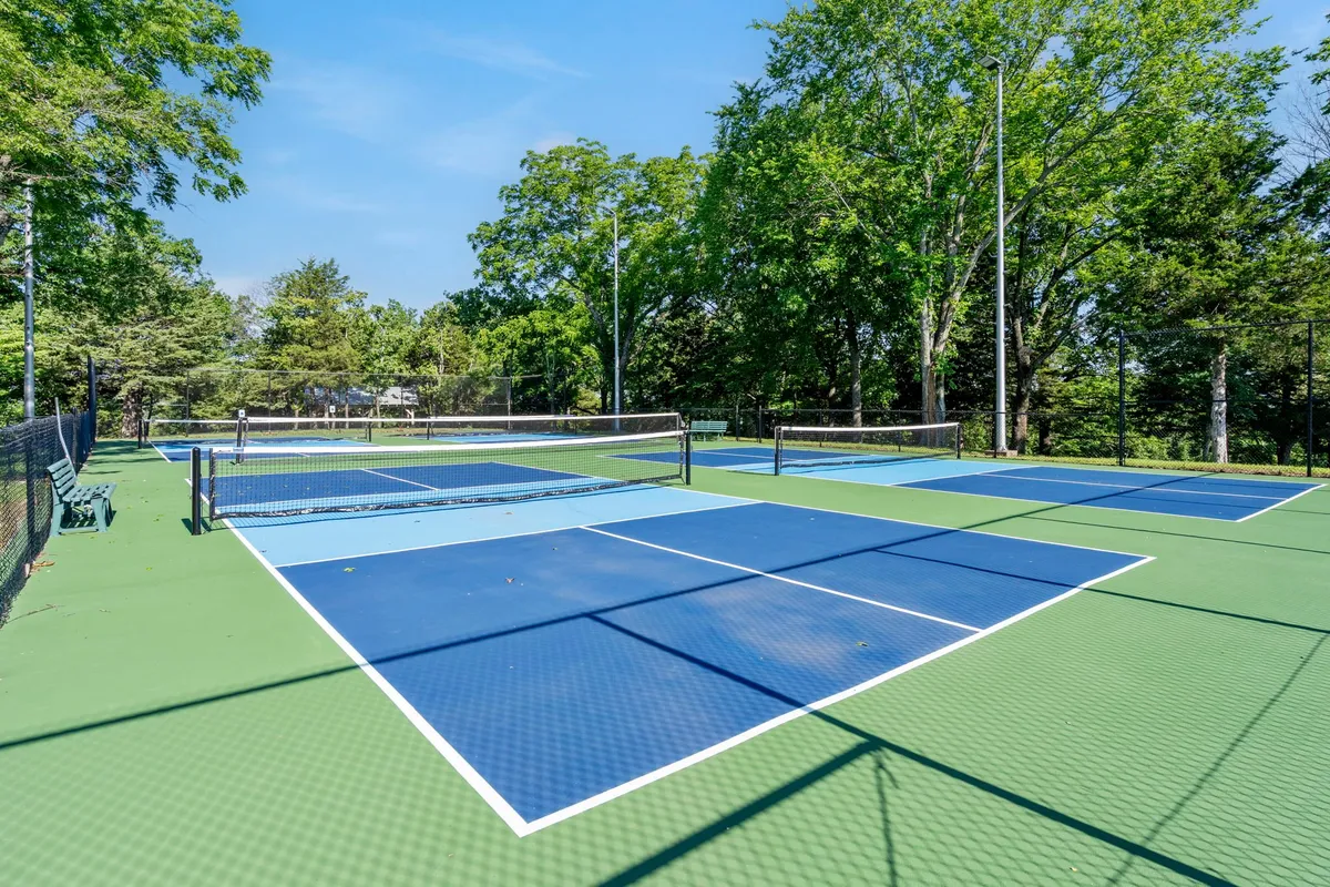 Outdoor tennis courts surrounded by netting and tall, leafy trees, bathed in bright sunshine. The courts invite guests to engage in energetic sports or friendly competition with travel companions.