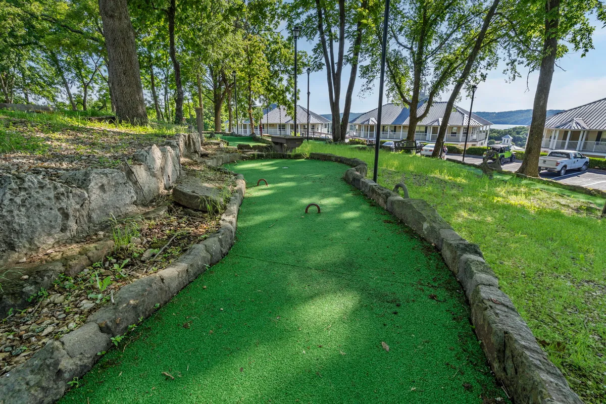 This image features a cheerful mini-golf course nestled among mature trees with inviting rock borders and open green space. The outdoor setting is vibrant and welcoming, ideal for family play and group activities.