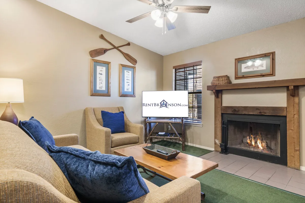 A warm, inviting living room centered around a stone fireplace, with a plush sofa, television, and decorative oars and artwork on the wall. The arrangement encourages group relaxation and conversation, making it ideal for gatherings after a day of activities.