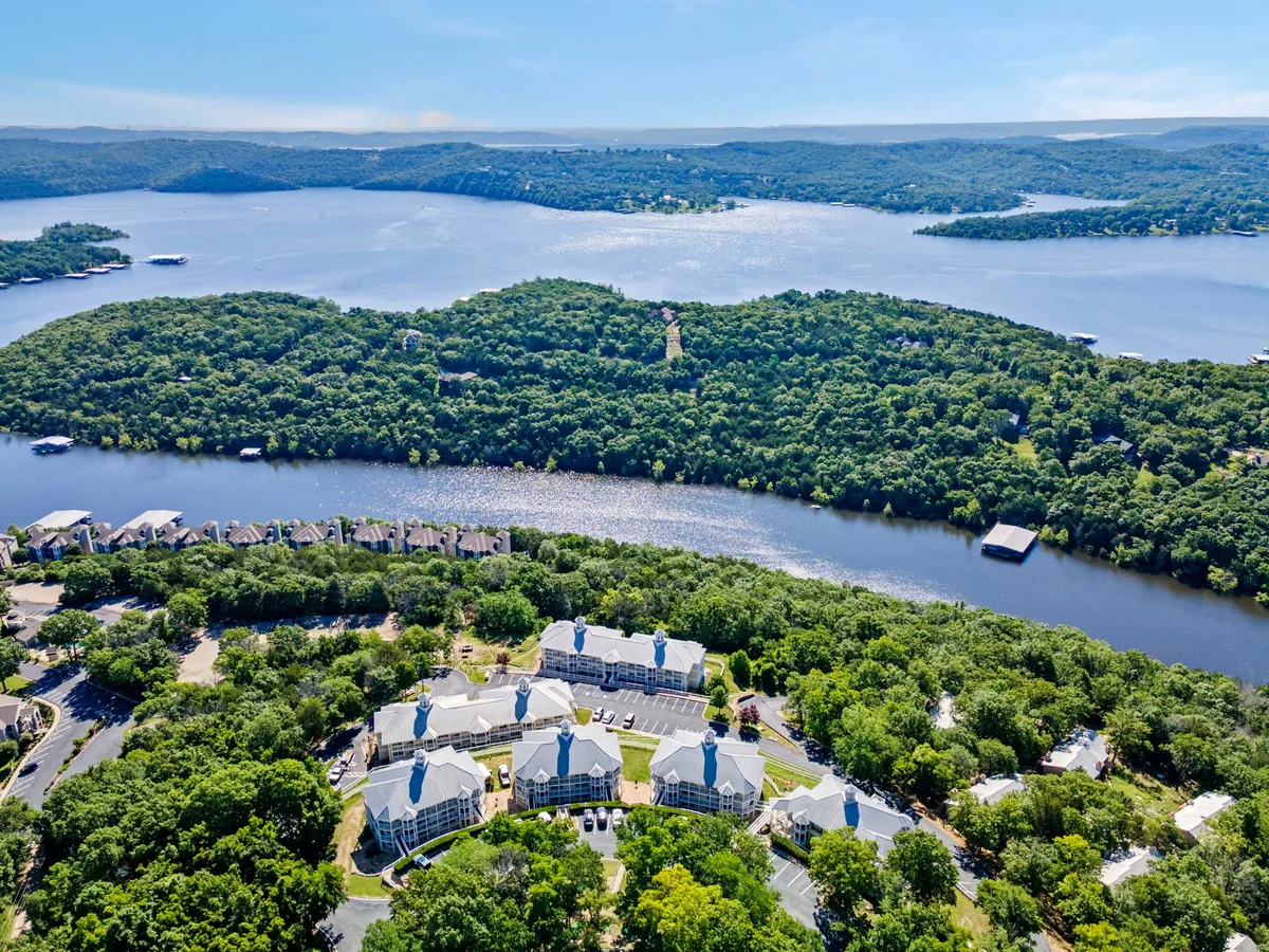 A panoramic view looking out over Table Rock Lake with gentle hills and residential buildings along the shore. The tranquil blue water and natural landscape suggest a perfect environment for boating, fishing, and lakeside relaxation.